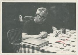 A candid photograph of Karmenu writing at a table