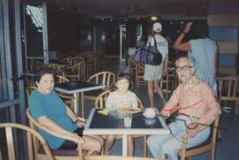 Karmenu sitting at a table with a woman and a young girl