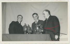 Gruppetta and two men behind vases or trophies on a table