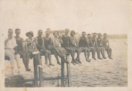A group of people sitting across a wooden pole in St George's Bay