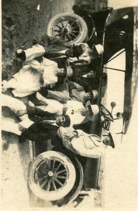 An unknown motor car with a group of 8 people